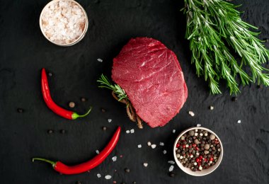 Siyah taş arka plan üzerinde yeşil biberiye dalları ve baharatlar ile Çiğ biftek 