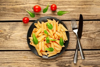 Ahşap arka plan üzerinde domates sosu ve yeşil yaprakları ile Makarna 