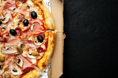 Siyah taş arka plan üzerinde kutusunda mantar, domates, zeytin ve jambon ile taze ev yapımı pizza