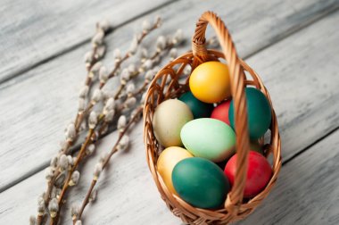 Beyaz ahşap arka planda renkli Paskalya yumurtaları ve kedi söğüt dalları ile sepet