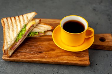 Jambon ve peynir ile taze ızgara sandviç ahşap doğrama tahtası üzerinde kahve fincan ile servis