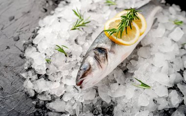 Soğuk ezilmiş buz yığını üzerinde limon dilimleri ve biberiye ile taze balık yakın görünümü
