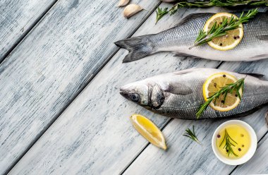 Gri ahşap arka plan üzerinde limon dilimleri ve biberiye dalları ile çiğ balık