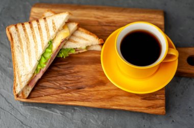 Jambon ve peynir ile taze ızgara sandviç ahşap doğrama tahtası üzerinde kahve fincan ile servis