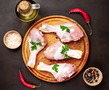 Siyah taş arka plan üzerinde ahşap doğrama tahtası üzerinde baharat, tuz, maydanoz yaprakları ve yağ şişesi ile Tavuk bacakları