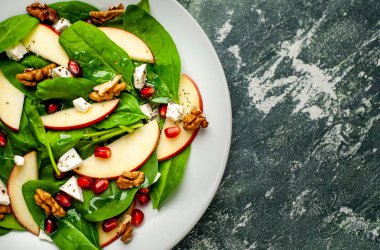 Ispanak yaprakları, peynir, nar tohumu, elma dilimleri ve taş arka plan üzerinde fındık ile taze salata 