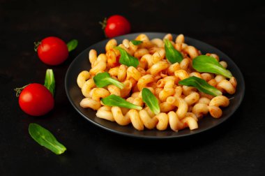 domates soslu makarna, yeşil yapraklar ve taş siyah arka plan üzerinde olgun domates