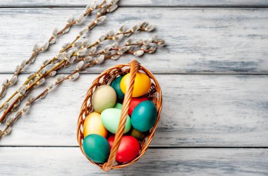 Beyaz ahşap arka planda renkli Paskalya yumurtaları ve kedi söğüt dalları ile sepet