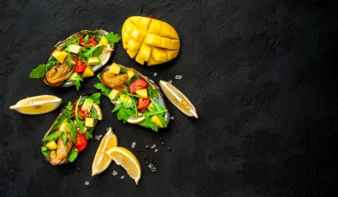 Siyah beton arka plan üzerinde avokado, arugula, mango, domates ve limon dilimleri ile pişmiş midye