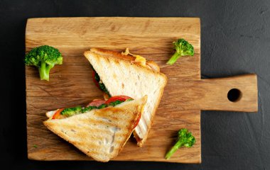 Ahşap doğrama tahtasında jambon, taze brokoli ve peynirile taze ızgara sandviçler