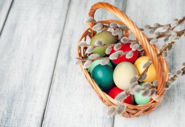 Beyaz ahşap arka planda renkli Paskalya yumurtaları ve kedi söğüt dalları ile sepet