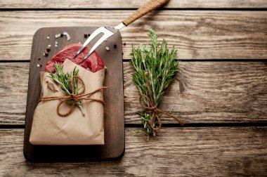 Ahşap doğrama tahtası üzerinde biberiye dalları ile zanaat kağıt sarılmış çiğ sığır eti biftek