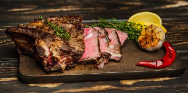 Taze kavrulmuş biftek ahşap doğrama tahtası üzerinde limon dilimleri ve ızgara sarımsak ile servis