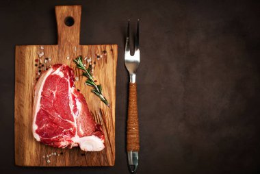 Taş arka plan üzerinde ahşap doğrama tahtası üzerinde baharat ve biberiye dal ile Çiğ yağlı biftek