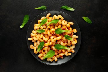 taş siyah arka plan üzerinde yeşil yaprakları ile servis domates soslu makarna