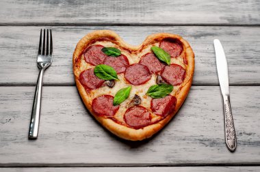 ahşap arka plan üzerinde salam ve taze fesleğen yaprakları ile peynir kalp pizza