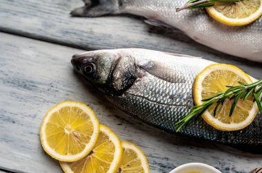 Gri ahşap arka plan üzerinde limon dilimleri ve biberiye dalları ile çiğ balık