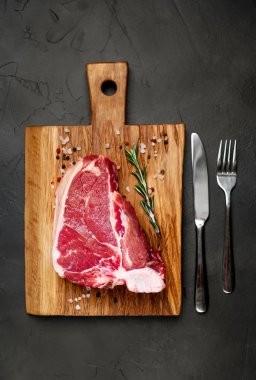 Taş arka plan üzerinde ahşap doğrama tahtası üzerinde baharat ve biberiye dal ile Çiğ yağlı biftek