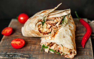 Geleneksel Meksika burrito tavuk ve sebze ile sarılmış ahşap doğrama tahtası üzerinde olgun domates ile servis 