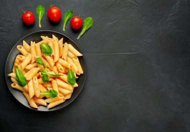 domates soslu makarna, yeşil yapraklar ve taş siyah arka plan üzerinde olgun domates