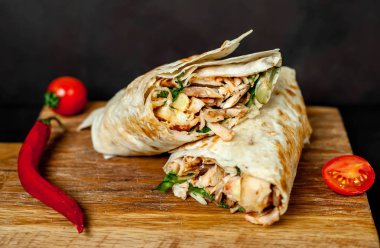 Geleneksel Meksika burrito tavuk ve sebze ile sarılmış ahşap doğrama tahtası üzerinde olgun domates ile servis 