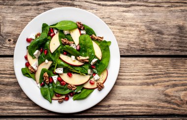 Ahşap arka plan üzerinde ıspanak yaprakları, peynir, nar tohumu, elma dilimleri ve fındık ile taze salata 