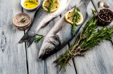 Gri ahşap arka plan üzerinde limon dilimleri ve biberiye dalları ile çiğ balık