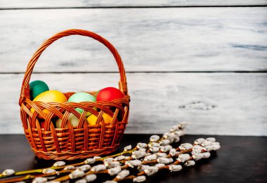 Beyaz ahşap arka planda renkli Paskalya yumurtaları ve kedi söğüt dalları ile sepet