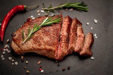 Siyah taş arka plan üzerinde baharat ve biberiye dalları ile Taze ızgara domuz biftek