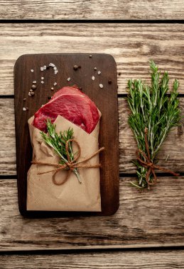 Ahşap doğrama tahtası üzerinde biberiye dalları ile zanaat kağıt sarılmış çiğ sığır eti biftek