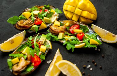Siyah beton arka plan üzerinde avokado, arugula, mango, domates ve limon dilimleri ile pişmiş midye
