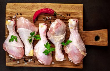 Ahşap doğrama tahtası üzerinde baharat, biber ve maydanoz yaprakları ile Tavuk bacakları 