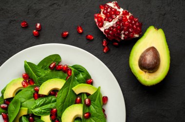 Ispanak yaprakları, avokado dilimleri ve taş masada nar taneleri ile taze yeşil salata 