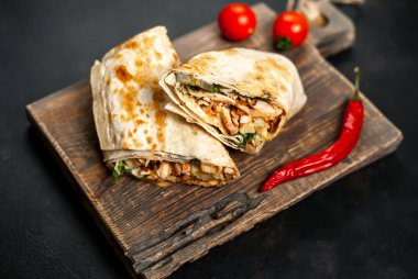 Geleneksel Meksika burrito tavuk ve sebze ile sarılmış ahşap doğrama tahtası üzerinde olgun domates ile servis 