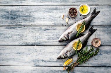 Gri ahşap arka plan üzerinde limon dilimleri ve biberiye dalları ile çiğ balık