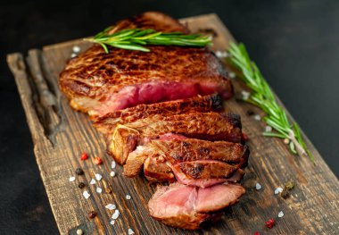 Ahşap tahta üzerinde biberiye dalları ile taze dilimlenmiş orta nadir sığır eti biftek