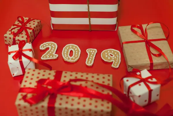 Parlak kırmızı arka plan üzerinde kırmızı yay ve 2019 çerezleri ile hediye kutuları yığını 