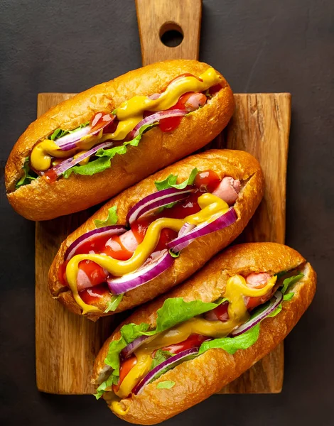 Fresh homemade hot-dogs with vegetables and sauces on wooden board