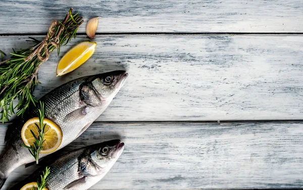 Gri ahşap arka plan üzerinde limon dilimleri ve biberiye dalları ile çiğ balık