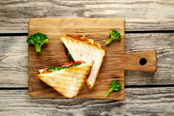 Ahşap doğrama tahtasında jambon, taze brokoli ve peynirile taze ızgara sandviçler