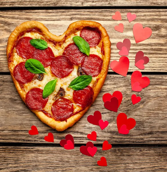 cheese heart pizza with salami and fresh basil leaves on wooden background with heart shape red confetti