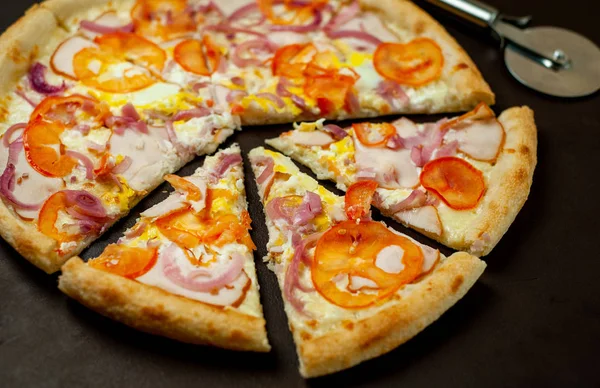 Fresh vegetable pizza with ham on black stone background