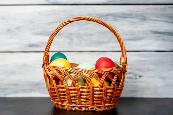Beyaz ahşap arka plan üzerinde renkli Paskalya ile sepet yumurta