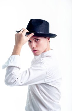 Beyaz gömlekli, siyah şapkalı, beyaz arka planda poz veren esmer bir genç. 