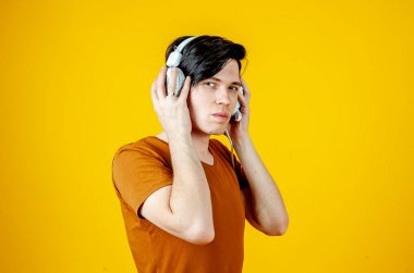 Young hipster man in headphones on bright yellow background 