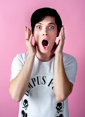 Genç esmer adam pastel pembe arka planda poz veriyor.