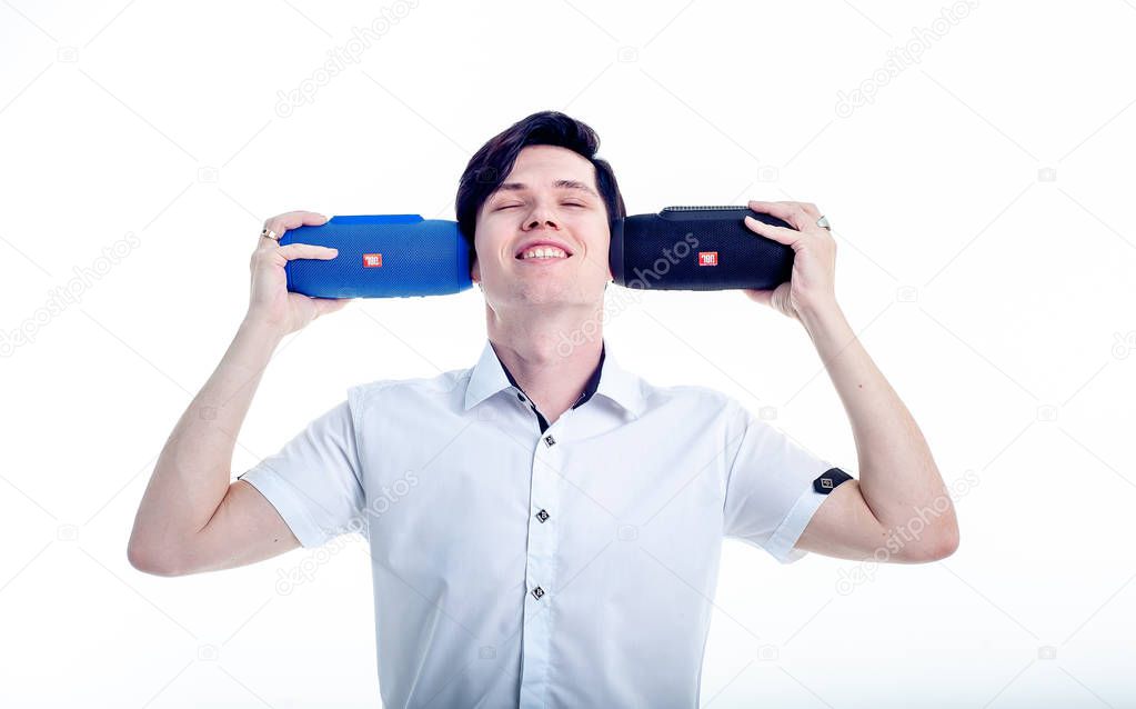 Young brunette man in white shirt holding two wireless speakers on white background 