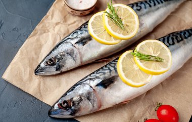 Siyah taş arka plan üzerinde limon dilimleri ve biberiye dalları ile çiğ balık