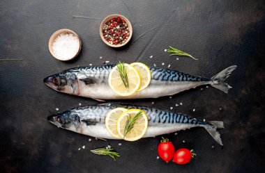 Siyah taş arka plan üzerinde limon dilimleri ve biberiye dalları ile çiğ balık