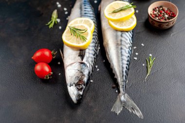 Siyah taş arka plan üzerinde limon dilimleri ve biberiye dalları ile çiğ balık